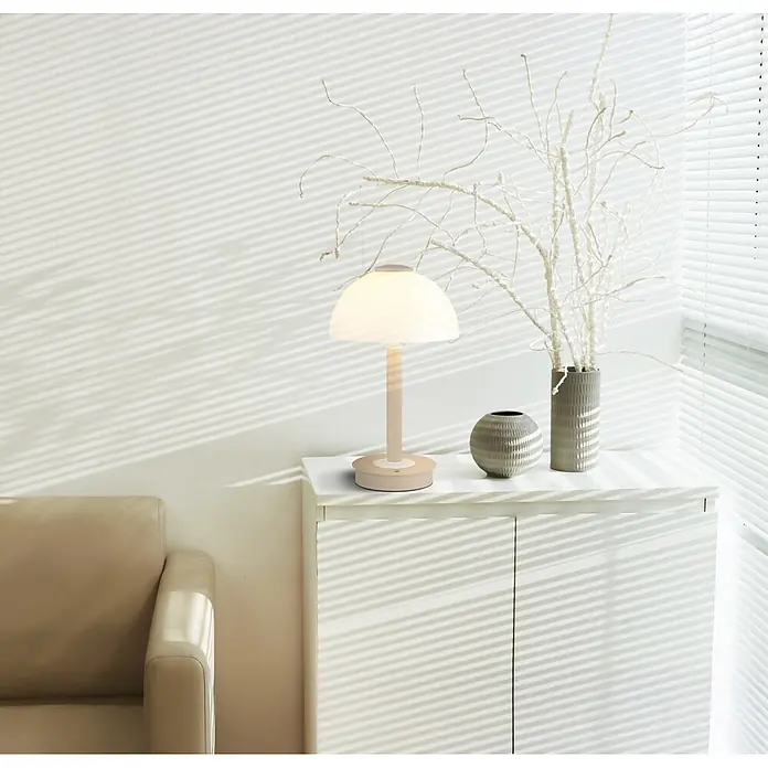 Globo LED-Tischleuchte Uldin - 7 W, Warmweiß - Cremefarbene Tischleuchte mit Kuppelschirm, die ein sanftes Licht auf einem weißen Schrank in einem hellen Raum abgibt.
