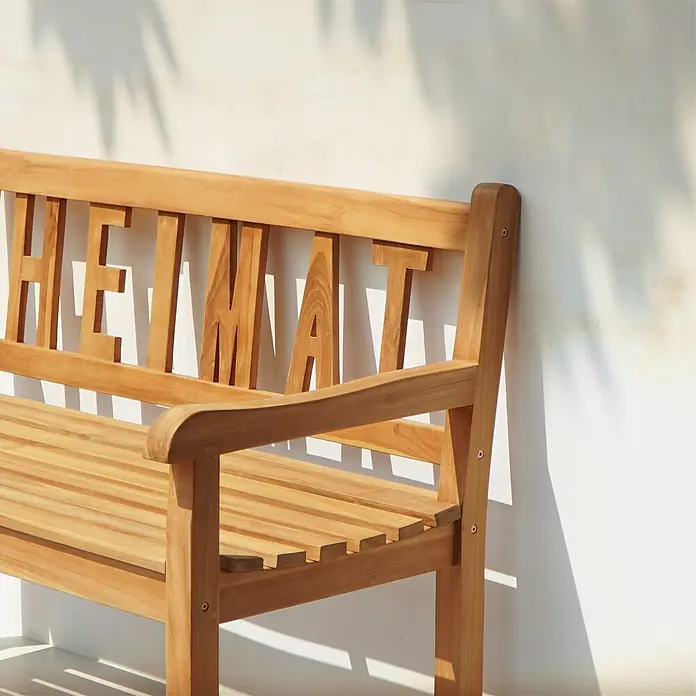 Garden Pleasure Gartenbank Heimat - B x T x H: 120 x 64 x 89 cm, Teak, Braun - Helle Holzbank mit der Aufschrift "HEIMAT" in der Rückenlehne, draußen im Sonnenlicht.