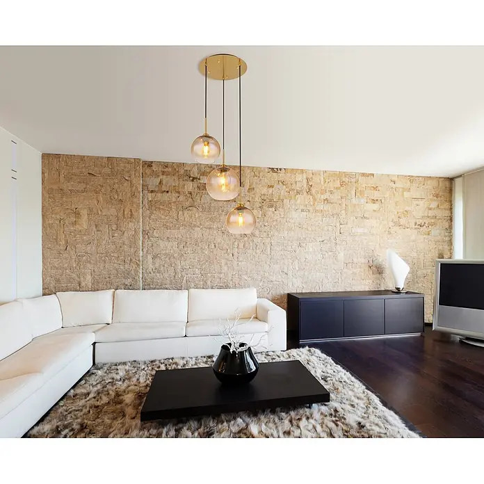 Globo Pendelleuchte Jamessa - 60 W, Ø x H: 35 x 150 cm, E27 - Moderne goldene Pendelleuchte mit drei bernsteinfarbenen Glaskugeln, die ein Wohnzimmer mit Steinwand und weißem Sofa beleuchtet.