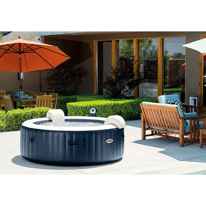 Intex Pure Spa Mobil-Whirlpool 85 Bubble MassageØ x H: 216 x 71 cm, Navy, 1.098 l - Ein Intex Whirlpool im Garten. Der Whirlpool ist blau und weiß und steht auf einer Terrasse. Sonnenschirme und Gartenmöbel sind ebenfalls zu sehen.