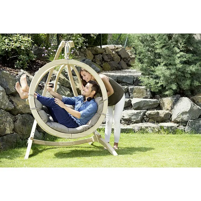 Amazonas Hängesessel Globo Chair - L x B x H: 69 x 118 x 121 cm, Natur/Taupe - Ein Mann und eine Frau genießen einen Hängekorb-Schaukelstuhl im Garten. Der Stuhl mit weichen Kissen bietet Komfort und Entspannung im Freien.