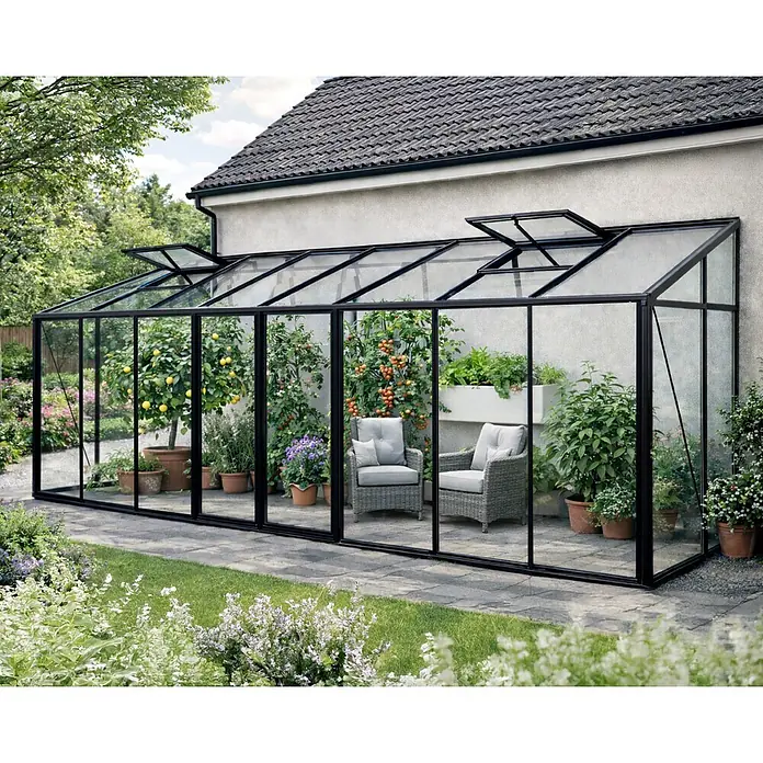 Bloomcabin Gewächshaus Aluminium Wandgewächshaus - Außenmaß inkl. Dachüberstand (B x T): 608 x 160 cm, Höhe: 268 cm, Material Seitenwand: Glas, 4 mm, Schwarz - Schwarz gerahmtes Anlehngewächshaus am Haus, gefüllt mit Pflanzen und zwei Stühlen, als gemütlicher Gartenraum.