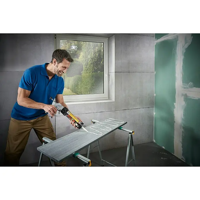 Wolfcraft Kartuschenpresse MG 611 - Geeignet für: Acryl - Ein Mann trägt Klebstoff mit der Klebepistole auf eine graue Platte auf. Die Platte steht auf einer Werkbank.