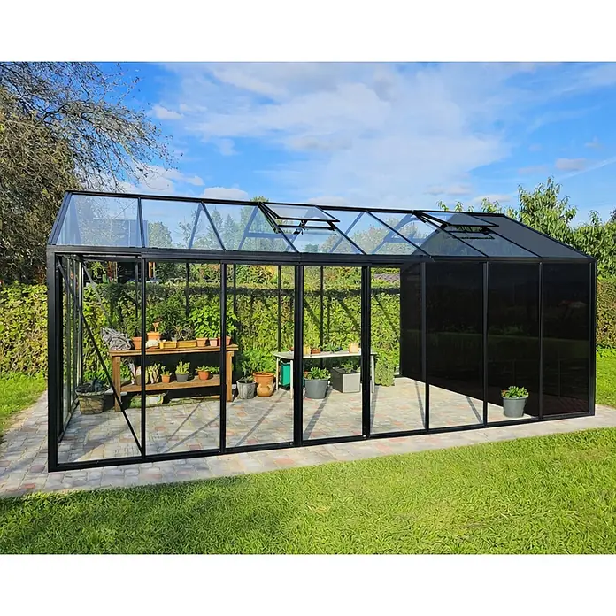 Bloomcabin Gewächshaus Aluminium Klassik mit kleinem integrierten Stauraum - Außenmaß inkl. Dachüberstand (B x T): 309 x 608 cm, Material Seitenwand: Glas, 4 mm, Schwarz - Großes, schwarzgerahmtes Gewächshaus im Garten mit klaren Glas- und Schattierungsbereichen sowie Pflanzen.