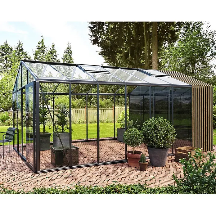 Bloomcabin Gewächshaus Aluminium Klassik mit Accoya-Fusion und kleinem integrierten Stauraum - Außenmaß inkl. Dachüberstand (B x T): 309 x 533 cm, Material Seitenwand: Glas, 4 mm, Schwarz - Modernes Gewächshaus mit schwarzem Rahmen, Glas und Holzlamellen auf einer Ziegelterrasse mit Pflanzen.