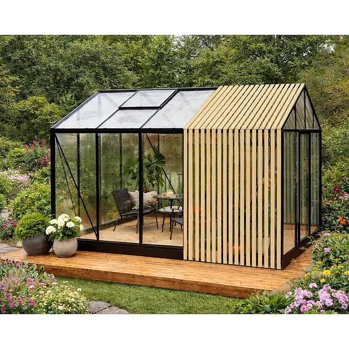Bloomcabin Gewächshaus Aluminium Limited Edition mit Accoya-Fusion - Außenmaß inkl. Dachüberstand (B x T): 235 x 384 cm, Material Seitenwand: Glas, 4 mm, Schwarz - Modernes Gewächshaus mit schwarzem Rahmen und Glas, ergänzt durch einen Naturholz-Lattenbereich. Es steht auf einer Holzterrasse in einem Garten mit sichtbaren Sitzgelegenheiten.