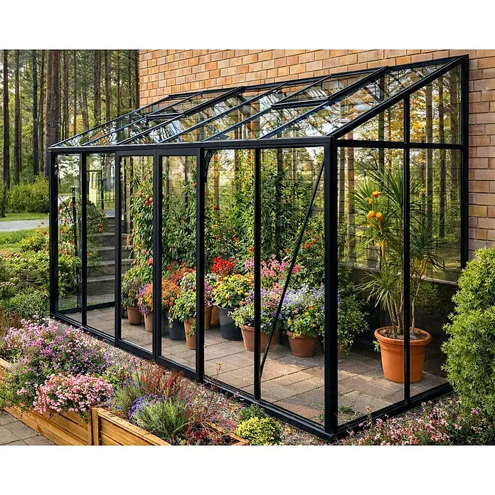 Bloomcabin Gewächshaus Aluminium Wandgewächshaus - Außenmaß inkl. Dachüberstand (B x T): 459 x 160 cm, Höhe: 268 cm, Material Seitenwand: Glas, 4 mm, Schwarz - Schwarz gerahmtes Glasgewächshaus an einem Backsteinhaus, gefüllt mit bunten Topfpflanzen und Blumen im Garten.