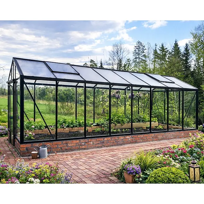 Bloomcabin Gewächshaus Aluminium für die Wandbasis - Außenmaß inkl. Dachüberstand (B x T): 235 x 608 cm, Material Seitenwand: Glas, 4 mm, Schwarz - Ein schwarz gerahmtes Gewächshaus mit transparenten Scheiben und einem Ziegelsockel, in einem blühenden Garten auf einem Ziegelweg.