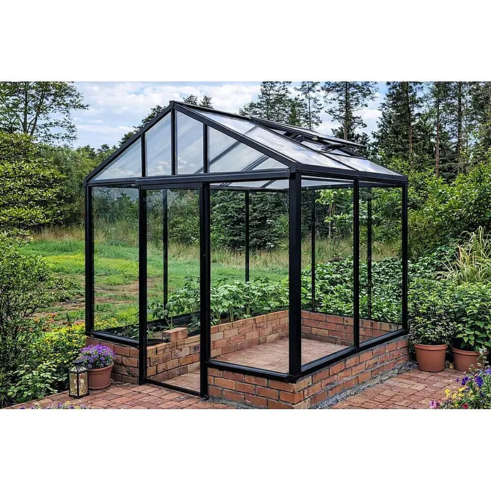 Bloomcabin Gewächshaus Aluminium für die Wandbasis - Außenmaß inkl. Dachüberstand (B x T): 235 x 160 cm, Material Seitenwand: Glas, 4 mm, Schwarz - Schwarz gerahmtes Gewächshaus mit Glaspaneelen und Ziegelsockel, mit Dachlüftern und Pflanzen, in einem grünen Garten.