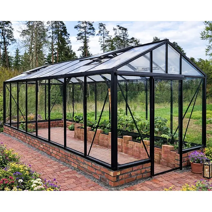 Bloomcabin Gewächshaus Aluminium für die Wandbasis - Außenmaß inkl. Dachüberstand (B x T): 235 x 608 cm, Material Seitenwand: Glas, 4 mm, Schwarz - Großes Gewächshaus mit schwarzem Rahmen und Glaswänden auf einem Ziegelsockel, mit Pflanzen darin und Ziegelweg im Garten.