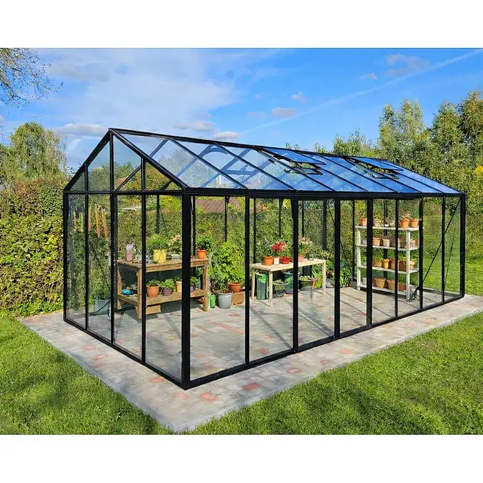 Bloomcabin Gewächshaus Aluminium Klassik - Außenmaß inkl. Dachüberstand (B x T): 309 x 459 cm, Material Seitenwand: Glas, 4 mm, Schwarz - Großes, schwarz gerahmtes Glasgewächshaus mit Dachlüftern, Pflanzen und Regalen, auf gepflastertem Sockel im Garten.