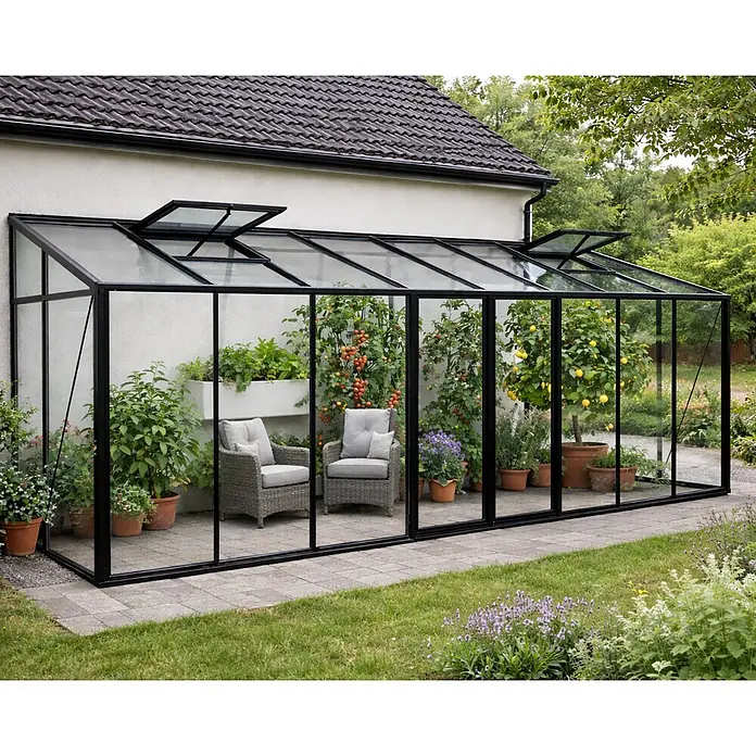 Bloomcabin Gewächshaus Aluminium Wandgewächshaus - Außenmaß inkl. Dachüberstand (B x T): 608 x 160 cm, Höhe: 251 cm, Material Seitenwand: Glas, 4 mm, Schwarz - Anlehngewächshaus mit schwarzem Rahmen und Glaspaneelen am Haus. Innen Pflanzen, Tomaten, Zitronen und zwei Rattanstühle.