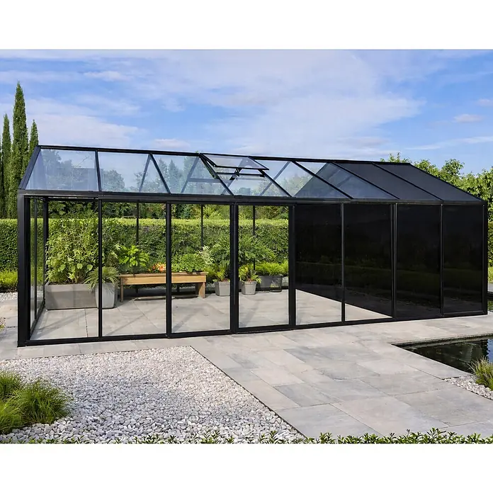 Bloomcabin Gewächshaus Aluminium Klassik mit mittlerem integrierten Stauraum - Außenmaß inkl. Dachüberstand (B x T): 235 x 608 cm, Material Seitenwand: Glas, 4 mm, Schwarz - Modernes schwarzes Glasgewächshaus mit Pflanzen, auf einer Terrasse neben einem Teich.