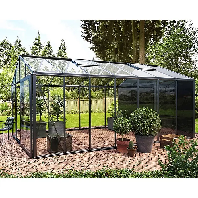 Bloomcabin Gewächshaus Aluminium Klassik mit kleinem integrierten Stauraum - Außenmaß inkl. Dachüberstand (B x T): 235 x 533 cm, Material Seitenwand: Glas, 4 mm, Schwarz - Großes schwarz gerahmtes Gewächshaus mit Klarglaswänden und Dachlüftern auf einer Ziegelterrasse im Garten.