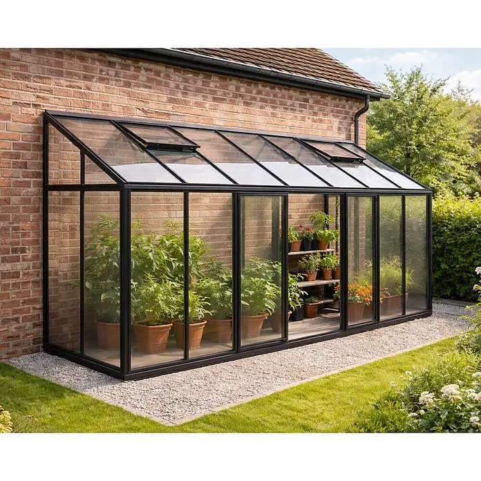Bloomcabin Gewächshaus Aluminium Wandgewächshaus - Außenmaß inkl. Dachüberstand (B x T): 533 x 160 cm, Höhe: 268 cm, Material Seitenwand: Glas, 4 mm, Schwarz - Anlehn-Gewächshaus mit schwarzem Rahmen und Glaspaneelen, an Ziegelwand, mit Topfpflanzen und Dachlüftern.