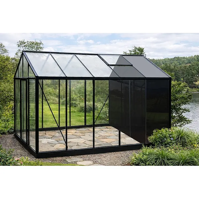 Bloomcabin Gewächshaus Aluminium Klassik mit kleinem integrierten Stauraum - Außenmaß inkl. Dachüberstand (B x T): 235 x 384 cm, Material Seitenwand: Glas, 4 mm, Schwarz - Modernes Gewächshaus mit schwarzem Rahmen, klaren und dunklen Paneelen, Steinboden, im Freien an einem See gelegen.