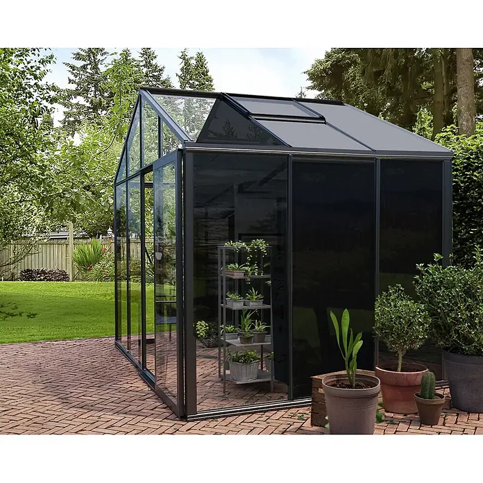 Bloomcabin Gewächshaus Aluminium Klassik mit mittlerem integrierten Stauraum - Außenmaß inkl. Dachüberstand (B x T): 309 x 235 cm, Material Seitenwand: Glas, 4 mm, Schwarz - Modernes dunkelgraues Gewächshaus mit Glaswänden und Dachlüftung auf einer Ziegelterrasse im Garten, beherbergt Topfpflanzen.