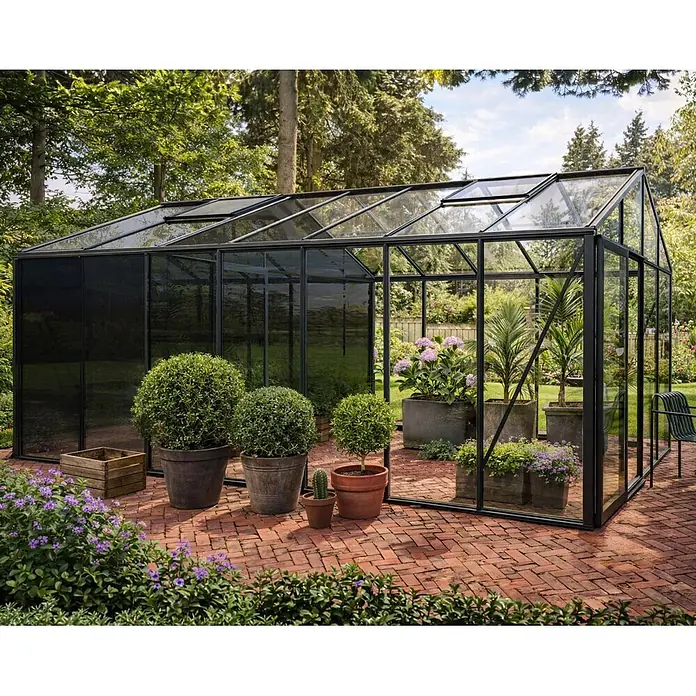 Bloomcabin Gewächshaus Aluminium Klassik mit mittlerem integrierten Stauraum - Außenmaß inkl. Dachüberstand (B x T): 309 x 533 cm, Material Seitenwand: Glas, 4 mm, Schwarz - Großes Gewächshaus mit schwarzem Rahmen und Glas auf einer Ziegelterrasse in einem üppigen Garten, zeigt diverse Topfpflanzen.