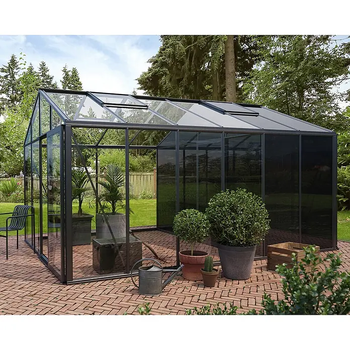 Bloomcabin Gewächshaus Aluminium Klassik mit mittlerem integrierten Stauraum - Außenmaß inkl. Dachüberstand (B x T): 309 x 459 cm, Material Seitenwand: Glas, 4 mm, Schwarz - Großes Gewächshaus aus schwarzgerahmtem Glas auf einer Ziegelterrasse in einem Garten, mit Pflanzen innen und außen.