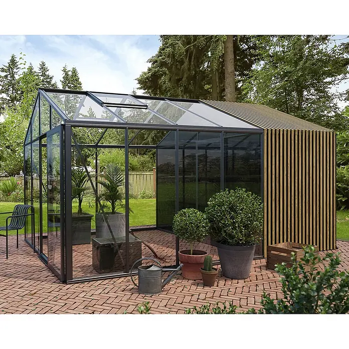 Bloomcabin Gewächshaus Aluminium Klassik mit Accoya-Fusion und mittlerem integrierten Stauraum - Außenmaß inkl. Dachüberstand (B x T): 309 x 459 cm, Material Seitenwand: Glas, 4 mm, Schwarz - Modernes Garten-Gewächshaus mit dunklem Metallrahmen, Glasplatten und einer Seite aus Holzlamellen, auf einer Ziegelterrasse.