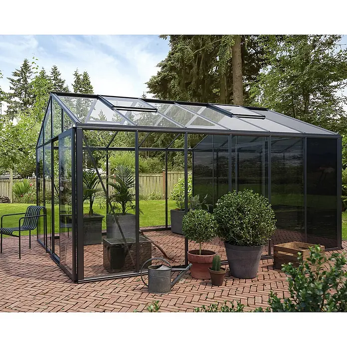 Bloomcabin Gewächshaus Aluminium Klassik mit kleinem integrierten Stauraum - Außenmaß inkl. Dachüberstand (B x T): 235 x 459 cm, Material Seitenwand: Glas, 4 mm, Schwarz - Geräumiges, modernes anthrazitfarbenes Gewächshaus mit transparenten Scheiben auf Ziegelterrasse im Garten, bepflanzt.