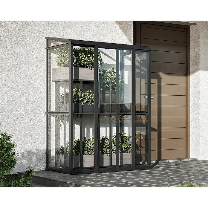 Bloomcabin Gewächshaus Aluminium Mini - Außenmaß inkl. Dachüberstand (B x T): 120 x 66 cm, Material Seitenwand: Glas, 4 mm, Schwarz - Hohes, schmales Gewächshaus mit schwarzem Rahmen und Glas, gefüllt mit Pflanzen, außen neben einem Gebäudeeingang platziert.