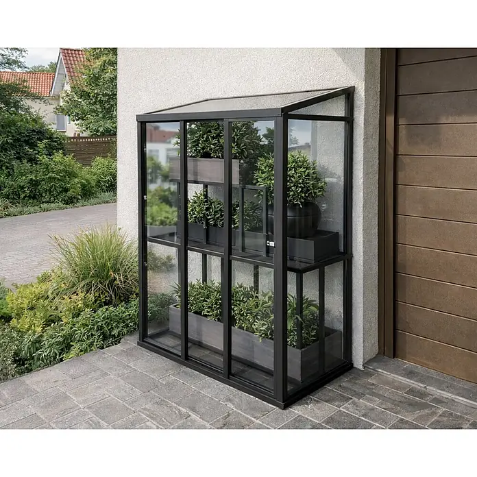 Bloomcabin Gewächshaus Aluminium Mini - Außenmaß inkl. Dachüberstand (B x T): 120 x 66 cm, Material Seitenwand: Glas, 4 mm, Schwarz - Hohes, schwarz gerahmtes Glasgewächshaus mit Regalen und Topfpflanzen, an eine Hauswand gelehnt.