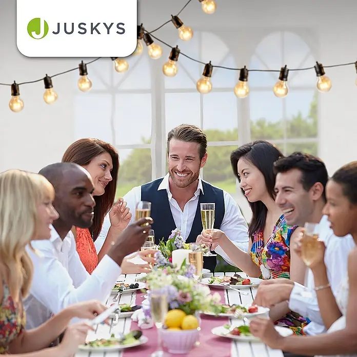 Juskys Partyzelt Gartenzelt - B x T: 300 x 600 cm, Farbe Dach: Weiß - Warmweiße Glühbirnen-Lichterkette mit schwarzem Kabel beleuchtet einen Esstisch im Freien, wo Menschen versammelt sind.