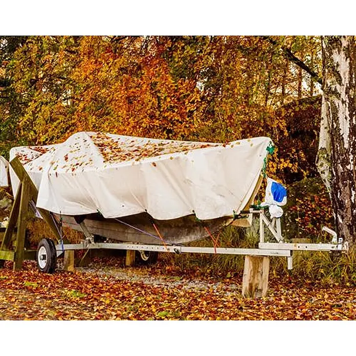 Aquagart Abdeckplane 260 4m x 6m Gewebeplane Abdeckplane - L x B: 4 x 6 m - Weiße Plane bedeckt ein Boot auf einem Trailer, draußen gelagert inmitten von Herbstlaub.