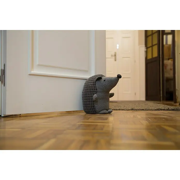Rei Tope de puerta Erizo - Textil - Un tope de puerta de erizo gris y tierno hecho de tela se encuentra frente a una puerta blanca para mantenerla abierta. El erizo tiene una nariz de botón.