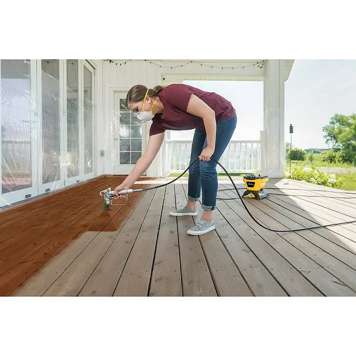Wagner High Efficiency Airless Farbsprühsystem Control 150 M - 350 W, Förderleistung: 0,9 l/min - Frau verwendet eine Farbspritzpistole, um eine Holzterrasse zu streichen. Die Farbspritzpistole ermöglicht eine gleichmäßige und effiziente Lackierung.