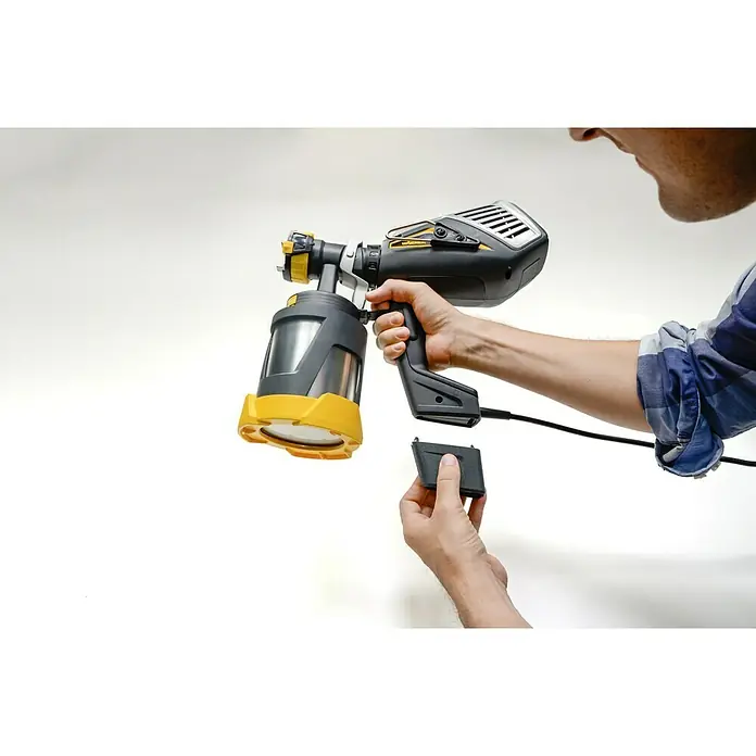 Wagner XVLP Farbsprühsystem FinishControl 3500 - 700 W - Eine Person hält eine Wagner Farbspritzpistole in der Hand, während sie eine schwarze Batterie anschließt. Das Gerät hat einen gelben Behälter.