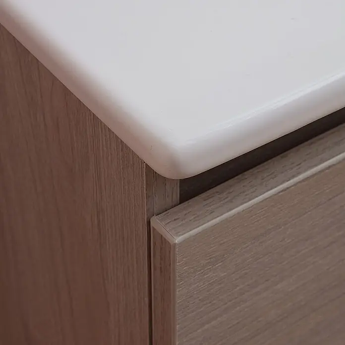 Kiamami Valentina Badmöbel-Set - Helles Holz - Ecke eines Badunterschranks mit weißer Waschtischplatte und hellem Holzdekor-Schrank mit Schublade.