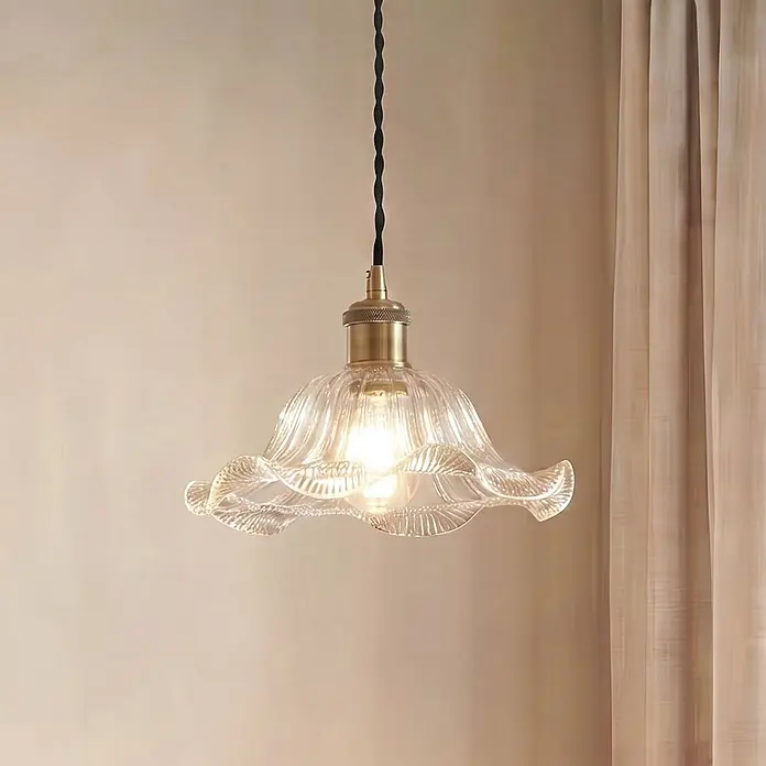 Lindby Pendelleuchte Ludowika - klar / transparent, transparent, messing, Schwarz, E27 - Klare Pendelleuchte aus geriffeltem Glas mit Messingfassung und schwarzem Textilkabel, hängt vor einer hellen Wand neben einem Vorhang.