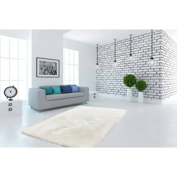 Kayoom Hochflorteppich Cosy - Weiß, 150 x 80 cm, 100 % Polyester - Ein weißer Teppich liegt in einem hellen Wohnzimmer mit grauer Couch und dekorativen Elementen. Die Einrichtung wirkt modern und einladend.