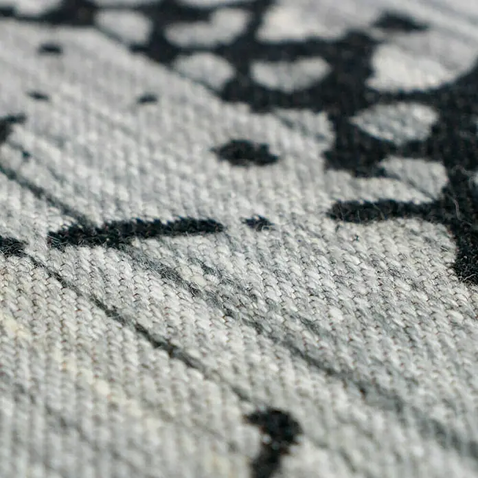 Kayoom Flachgewebeteppich Phönix - Natur/Creme, 290 x 200 cm, 75 % Wolle, 20 % Baumwolle, 5 % Polyester - Detailaufnahme eines grau-schwarzen Teppichs, der eine moderne und stilvolle Textur zeigt. Die Farbkombination bietet eine interessante Optik.