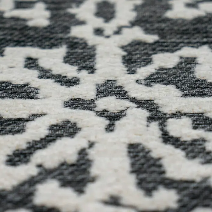 Kayoom Flachgewebeteppich River 130 - Anthrazit/Grau, 230 x 155 cm, 70 % Baumwolle, 30 % Polyester - Nahaufnahme eines grauen Teppichs mit weißem, floralem Muster. Der Teppich hat eine strukturierte Oberfläche.