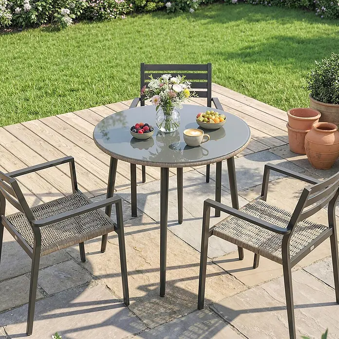 Outsunny Gartentisch rund - gehärtetes Glas, Grau - Eine Outdoor-Essgruppe aus dunkelgrauem Metalltisch mit grauer Glasplatte und Stühlen mit beigefarbenen geflochtenen Sitzen auf einer Terrasse.