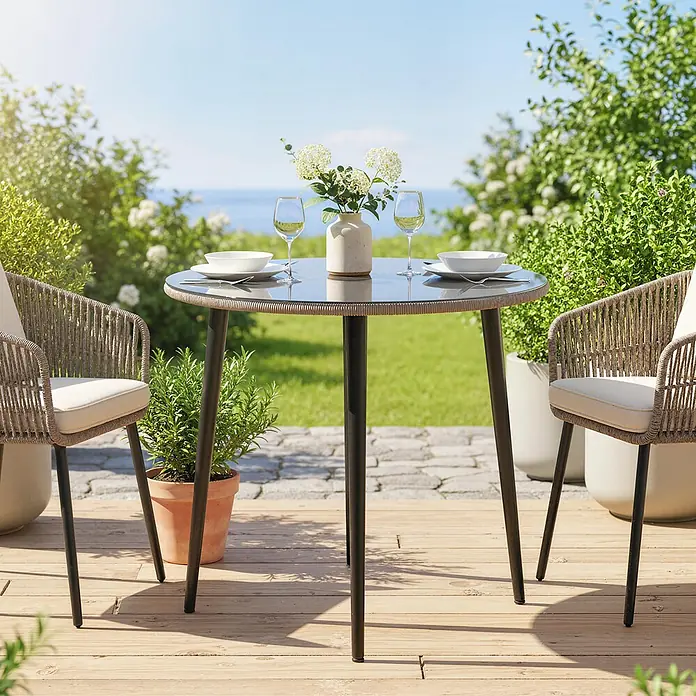 Outsunny Gartentisch rund - gehärtetes Glas, Grau - Outdoor-Esstisch-Set für zwei. Runder Tisch mit dunkler Glasplatte und geflochtenem Rand, zwei geflochtene Stühle mit cremefarbenen Kissen, auf Holzterrasse.
