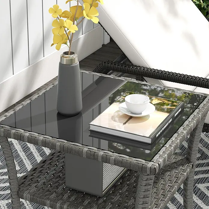 Outsunny Garten-Beistelltisch - L x B x H: 50 x 50 x 45 cm, PE-Rattan, Quadratisch, Grau - Grauer Rattan-Beistelltisch mit Glasplatte, neben einem Liegestuhl. Mit Vase, Buch, Tasse und Lautsprecher auf der unteren Ablage.
