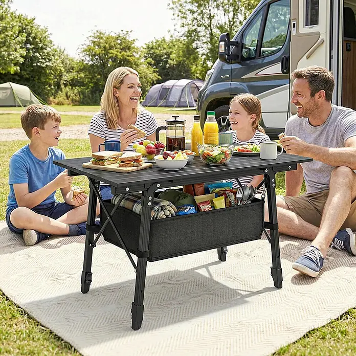 Outsunny Campingtisch - L x B x H: 90 x 55 x 66 cm, Oxford-Gewebe, Schwarz - Schwarzer tragbarer Campingtisch mit integriertem Stoff-Stauraumkorb, von einer Familie für ein Picknick genutzt.