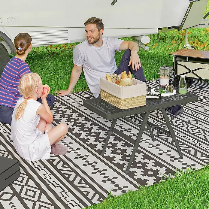 Outsunny Campingtisch - L x B x H: 90 x 40,5 x 58 cm, Schwarz - Familienpicknick mit einem dunkelgrauen klappbaren Outdoor-Tisch und einer schwarz-weiß gemusterten Matte.