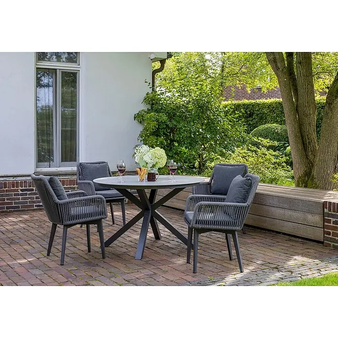 Bene Living Gartentisch-Set Marbella mit Tisch Almeria - Gesamtumfang: 5 -tlg., Gestell aus pulverbeschichtetem Aluminium, Tischplatte aus gesintertem Stein (Keramik), Bespannung aus Rope (Textilgemisch) - Dunkelgraue Outdoor-Essgruppe: runder Tisch mit sternförmigem Gestell, vier Stühle mit geflochtenen Lehnen und Kissen auf einer Terrasse.