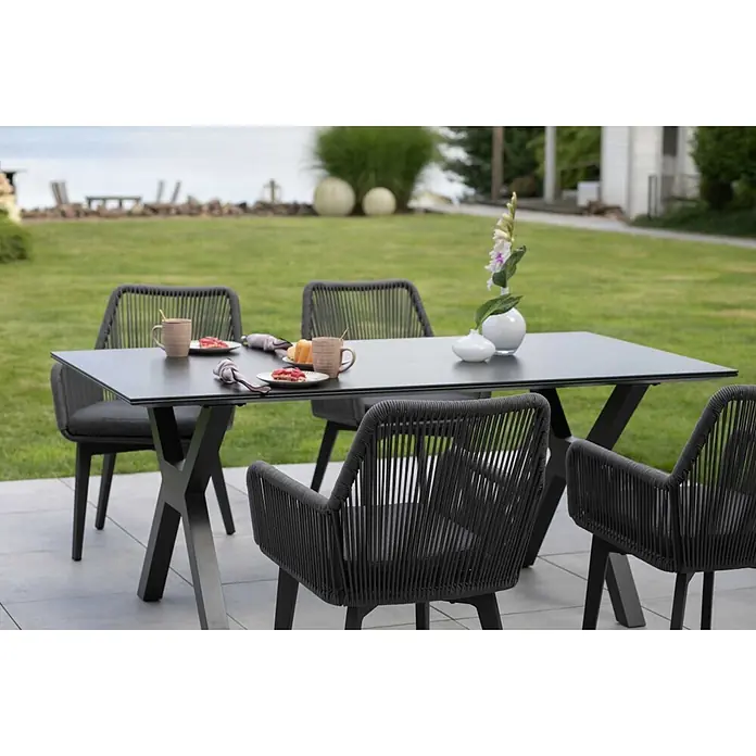 Bene Living Gartentisch-Set Marbella mit Tisch Granada - Gesamtumfang: 5 -tlg., Gestell aus pulverbeschichtetem Aluminium, Tischplatte aus gesintertem Stein (Keramik), Sitzfläche mit Rope-Bespannung (Textil/Kunststoffgemisch). - Dunkelgraue Outdoor-Essgruppe mit Rechtecktisch und geflochtenen Stühlen auf einer Terrasse, bereit zum Essen.