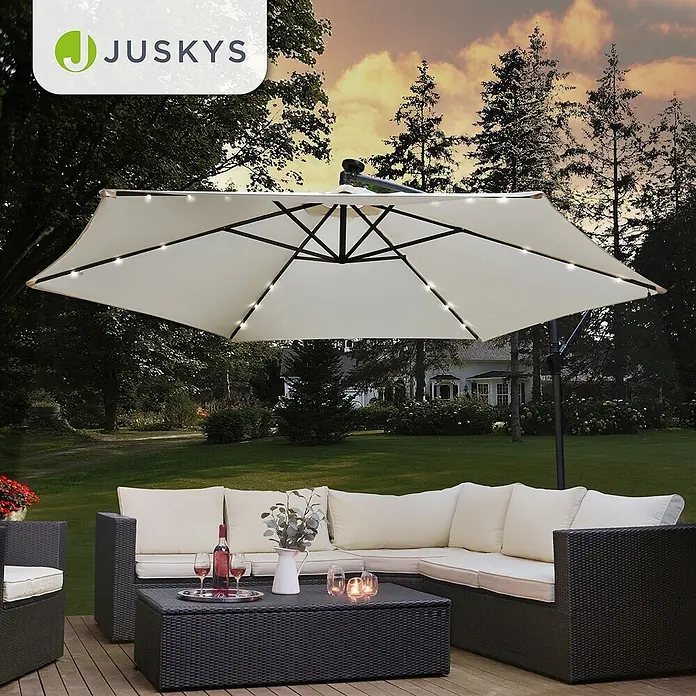 Juskys Ampelschirm rund Brazil inkl LED - creme, Durchmesser Bespannung: 300 cm - Dunkelbraune Rattan-Gartenmöbel mit cremefarbenen Kissen unter einem beigefarbenen Ampelschirm mit LED-Beleuchtung auf einer Terrasse.