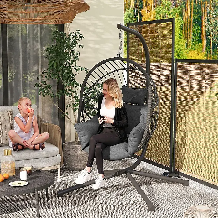 Furnicato Hängesessel - L x B x H: 120 x 106 x 188 cm, Polyester, Grau - Dunkelgrauer Hängesessel mit grauen Kissen, in dem eine Frau auf einer Terrasse entspannt.