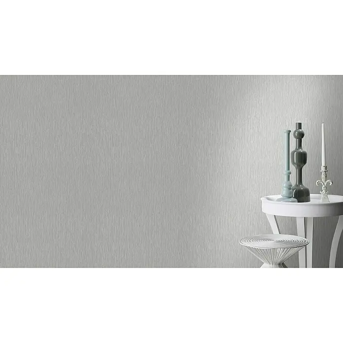 Rasch Trianon Vliestapete - Grau, Uni, 10,05 x 0,53 m - Ein elegantes silbernes Hintergrundbild mit vertikalen Texturen, neben dekorativen Elementen auf einem weißen Beistelltisch.