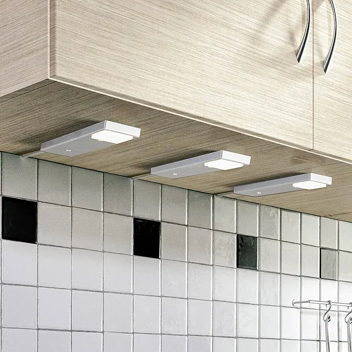 Lindby LED-Unterbauleuchte Amaryll -  - Drei silber-graue Unterschrankleuchten mit weißen Diffusoren, die eine geflieste Rückwand unter hellen Holzschränken beleuchten.