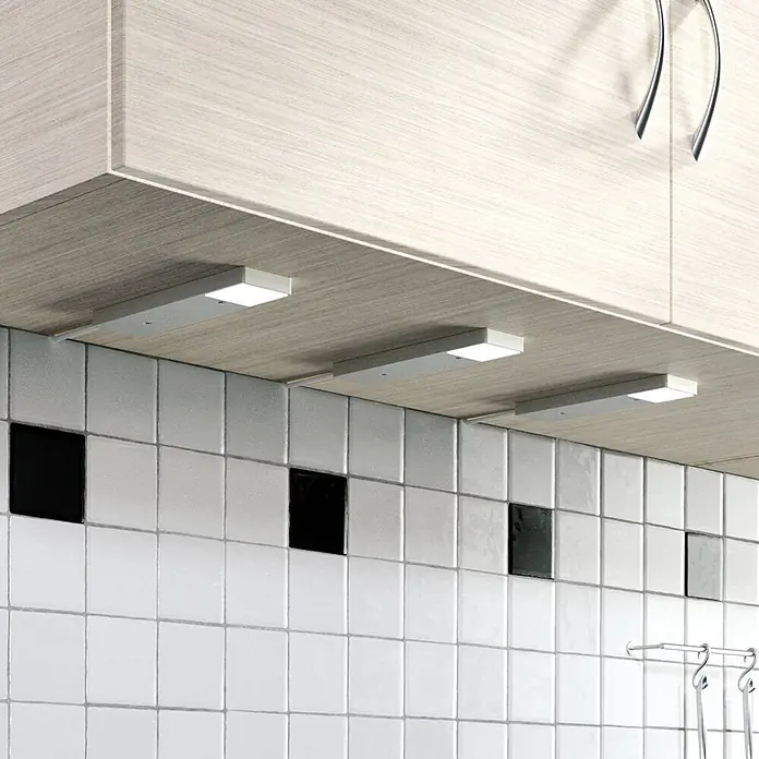 Lindby LED-Unterbauleuchte Amaryll -  - Drei silberne Unterbau-LED-Leuchten unter Holzküchenschränken, die die weiß geflieste Rückwand beleuchten.