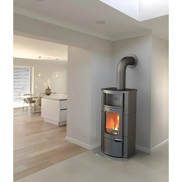 Kaminofen Prestige - 7 kW, Raumheizvermögen: 200 m³, Material Verkleidung: Stahl - Moderner, dunkelgrauer Holzofen mit sichtbarem Feuer in einem offenen Wohnbereich.